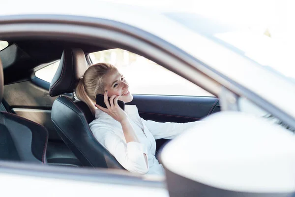 Hermosa mujer rubia conductor hablando teléfono inteligente al volante del coche — Foto de Stock