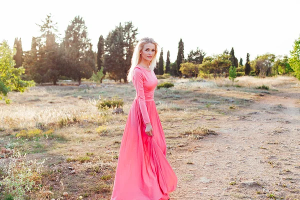 Hermosa mujer rubia en vestido rosa camina en el parque al atardecer —  Fotos de Stock