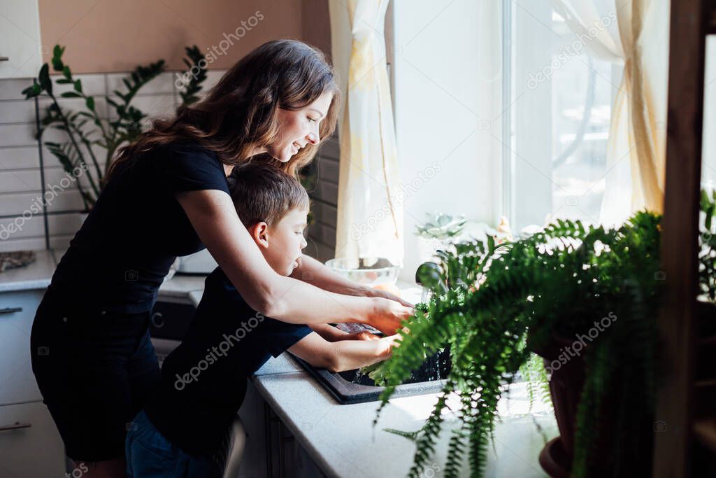 Mom with son wash vegetables in the kitchen