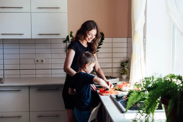 Mom and young son cut vegetables for salad in the kitchen — Stock Photo, Image