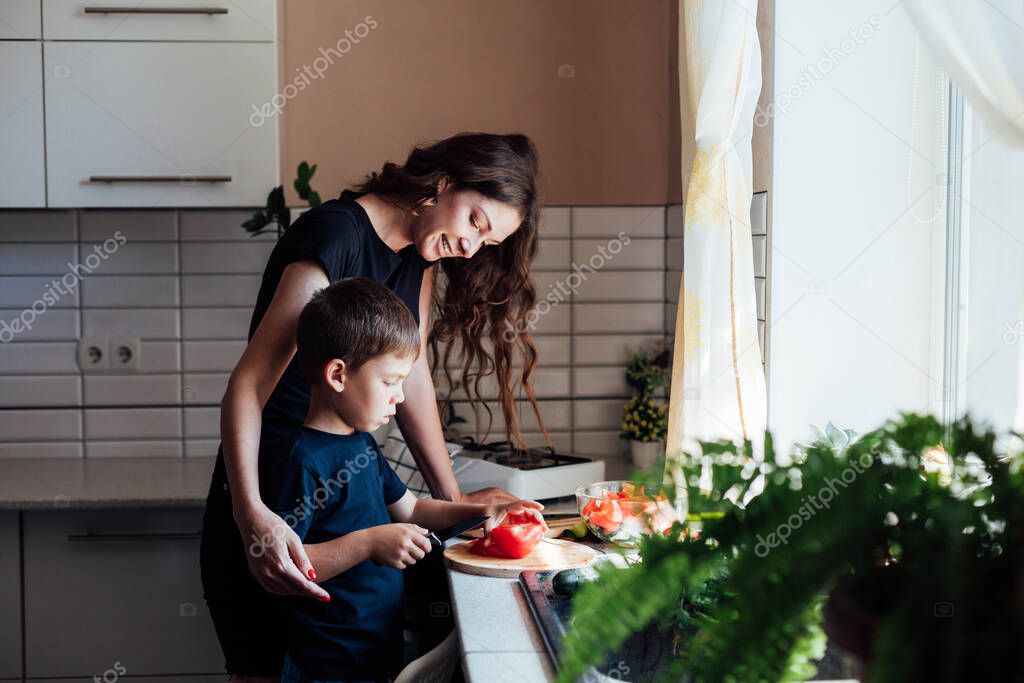 Mom and young son cut vegetables for salad in the kitchen
