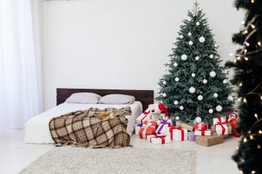 Süslü bir Noel ağacı olan, tavan arası tarzı geniş, beyaz bir yatak odası.