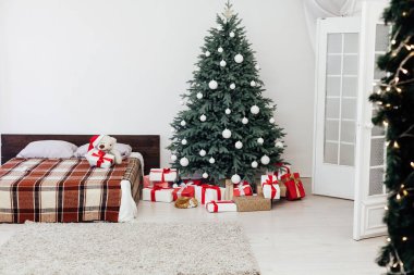 Süslü bir Noel ağacı olan, tavan arası tarzı geniş, beyaz bir yatak odası.