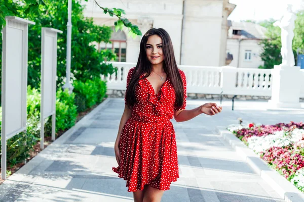 Kırmızı benekli elbiseli güzel esmer kadın şehrin sokaklarında yürüyor. — Stok fotoğraf