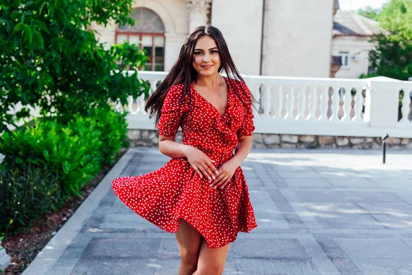 Krásná brunetka žena v červené puntíkové šaty procházky ulicemi města — Stock fotografie