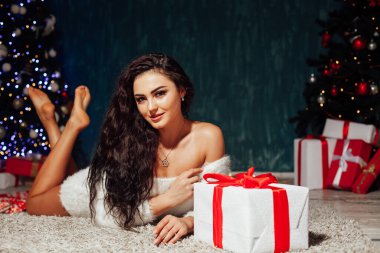 Güzel esmer kadın Noel ağacında çelenk ışıklarıyla hediyeleri açıyor.