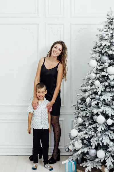 Мама и сын у белой елки с новогодними подарками — стоковое фото