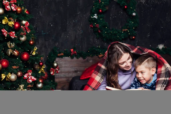 Mom reads a book to the boy to bed at the Christmas tree new year — Stock Photo, Image