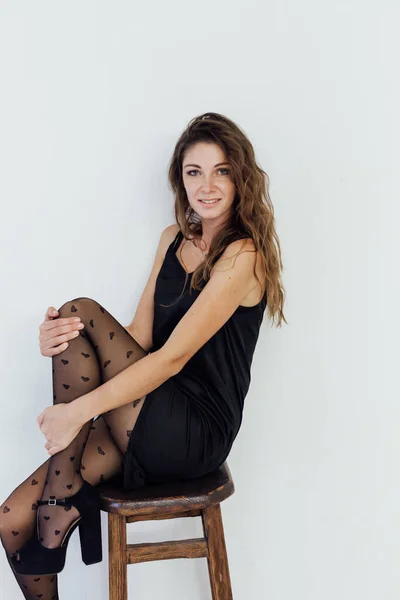 Mulher na moda bonita em vestido preto e meia-calça senta-se em uma cadeira — Fotografia de Stock