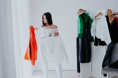 Giysi dolabından şık giysiler seçen mutlu, genç, gülümseyen esmer kadının portresi.