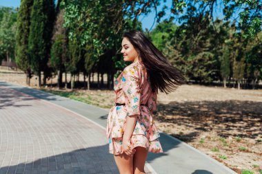 Çiçekli elbiseli güzel esmer kadın baharda parkta yürüyor.