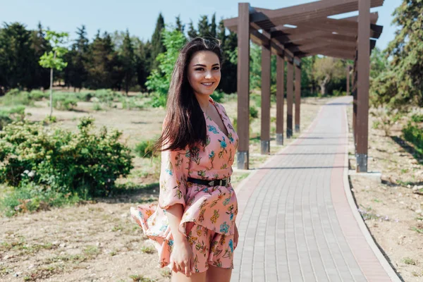 Mulher morena bonita em um vestido com flores caminha no parque na primavera — Fotografia de Stock