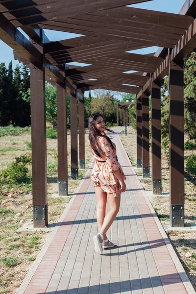 Mulher morena bonita em um vestido com flores caminha no parque na primavera — Fotografia de Stock