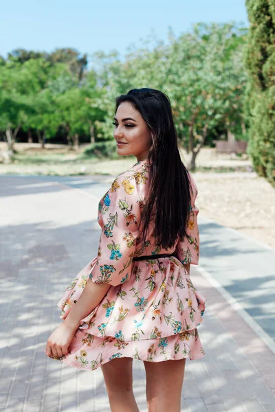 Schöne brünette Frau in einem Kleid mit Blumen spaziert im Frühling durch den Park — Stockfoto
