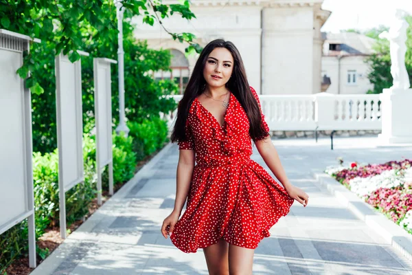 Mulher morena bonita em vestido de bolinhas vermelhas caminha pelas ruas da cidade — Fotografia de Stock