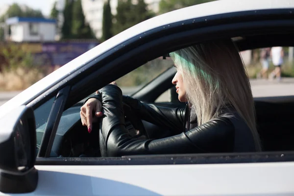 Hermosa mujer rubia de moda al volante de un coche blanco — Foto de Stock