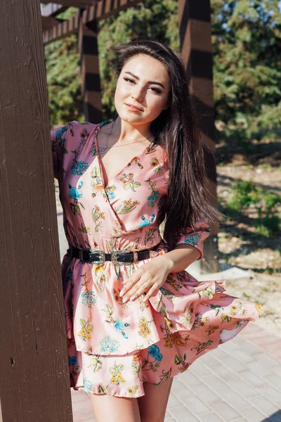 Beautiful fashionable brunette woman in a dress with flowers walks in the park on the street — Stock Photo, Image