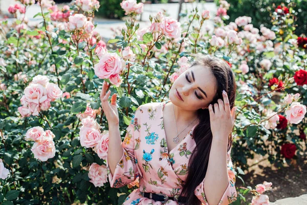 Hoş kokulu güllerin arasında çiçekli bir elbise giymiş güzel bir kadın. — Stok fotoğraf