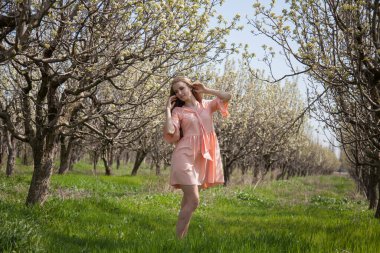 Çiçekli bahar yeşili bahçesinde pembe elbiseli güzel sarışın kadın.