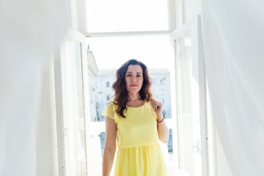 Pencerenin yanında sarı bir yaz elbisesi içinde güzel bir esmer kadının portresi.