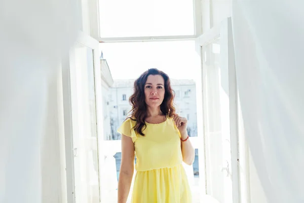 Porträt einer schönen brünetten Frau in einem gelben Sommerkleid am Fenster — Stockfoto