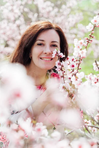 Çiçekli elbiseli güzel esmer kadın baharda çiçek açan bahçede yürüyor.