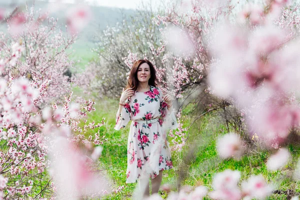 Çiçekli elbiseli güzel bir kadın baharda çiçek bahçesinde yürür. — Stok fotoğraf