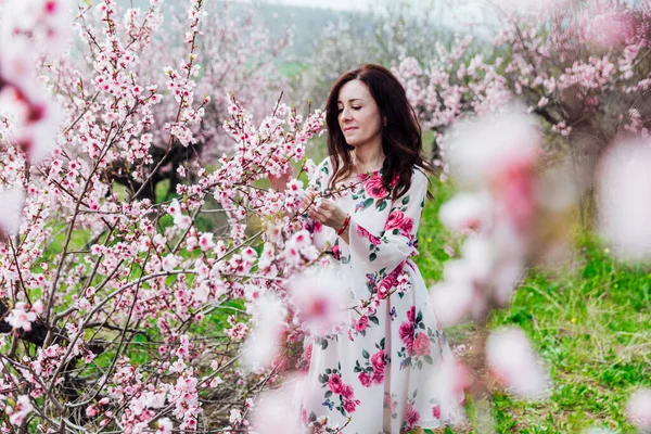 Mulher morena bonita em um vestido com flores em rosa florescendo pêssego jardim primavera — Fotografia de Stock