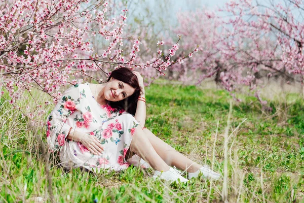 Mulher morena bonita em um vestido com flores em rosa florescendo pêssego jardim primavera — Fotografia de Stock