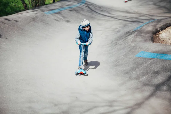 小さな男の子が遊び場の道路上のスクーターに乗る — ストック写真