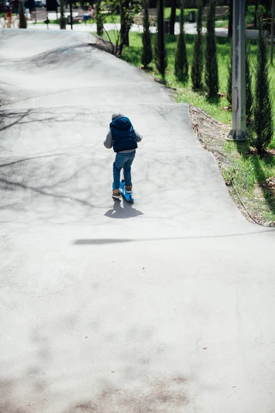 Ένα μικρό αγόρι οδηγεί ένα σκούτερ στους δρόμους στην παιδική χαρά — Φωτογραφία Αρχείου