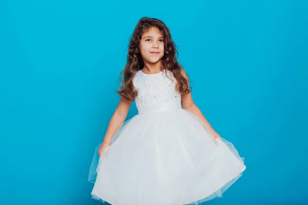 Belle petite fille bouclée de 5 ans dans une robe blanche sur fond bleu — Photo