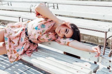 Çiçekli elbiseli güzel esmer kadın parkta yürüyor.