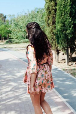 Çiçekli elbiseli güzel esmer kadın parkta yürüyor.