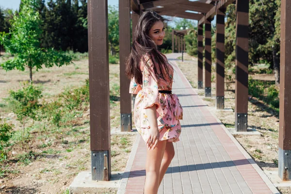 Çiçekli elbiseli güzel esmer kadın parkta yürüyor. — Stok fotoğraf