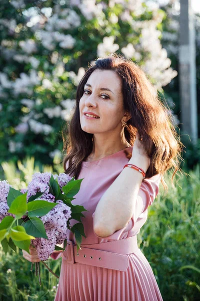 Retrato de uma bela mulher morena em um vestido lilás com flores lilás — Fotografia de Stock