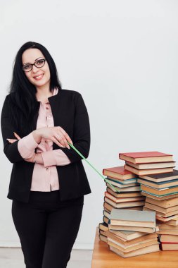 Sınıftaki güzel bayan öğretmen eğitim kitaplarıyla dolu bir masada.