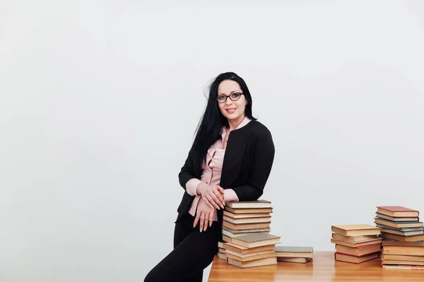 Bela professora em sala de aula em uma mesa com pilhas de livros educacionais — Fotografia de Stock