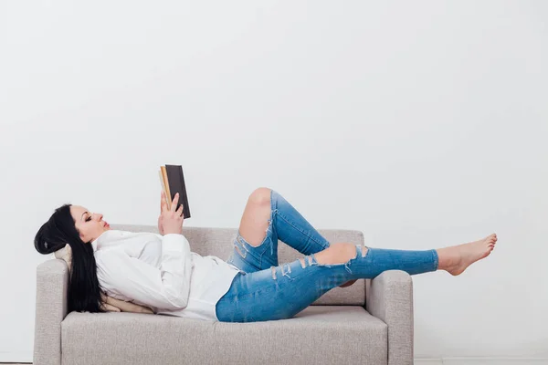 美しいですブルネット女性読みますA本に家でザカウチ — ストック写真