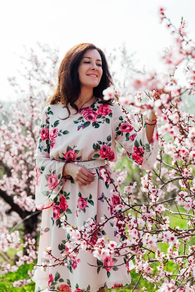 Belle femme brune dans une robe avec des fleurs se promène dans le jardin fleuri au printemps — Photo