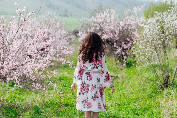 Çiçekli elbiseli güzel bir kadın baharda çiçek bahçesinde yürür. — Stok fotoğraf