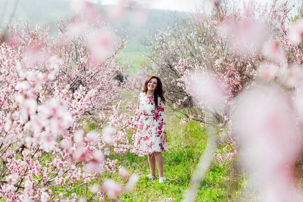 Çiçekli elbiseli güzel bir kadın baharda çiçek bahçesinde yürür. — Stok fotoğraf