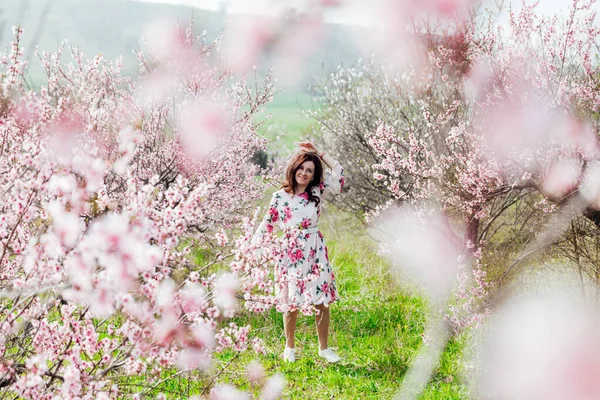 Çiçekli elbiseli güzel bir kadın baharda çiçek bahçesinde yürür. — Stok fotoğraf