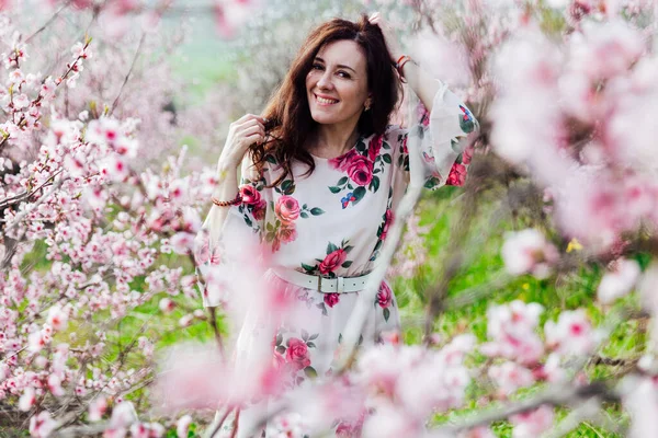 Mulher bonita em um vestido com flores caminha pelo jardim florido na primavera — Fotografia de Stock