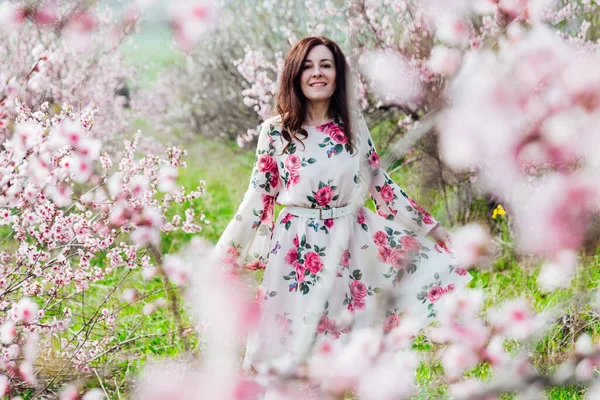 Piękna kobieta w sukience z kwiatami spaceruje wiosną po kwitnącym ogrodzie — Zdjęcie stockowe