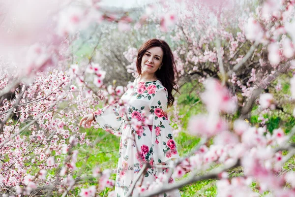 Mulher bonita em um vestido com flores caminha pelo jardim florido na primavera — Fotografia de Stock