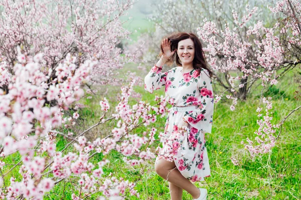 Belle femme brune dans une robe avec des fleurs en rose floraison pêcher jardin printemps — Photo