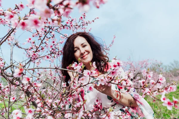 Mulher morena bonita em um vestido com flores em rosa florescendo pêssego jardim primavera — Fotografia de Stock