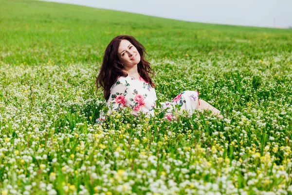 Çiçekli güzel esmer kadın bahar tarlasında oturuyor. — Stok fotoğraf