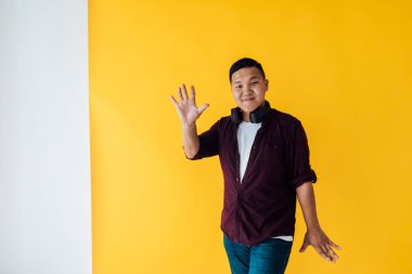 Asyalı adam sarı arka planda kulaklıkla müzik eşliğinde dans ediyor.